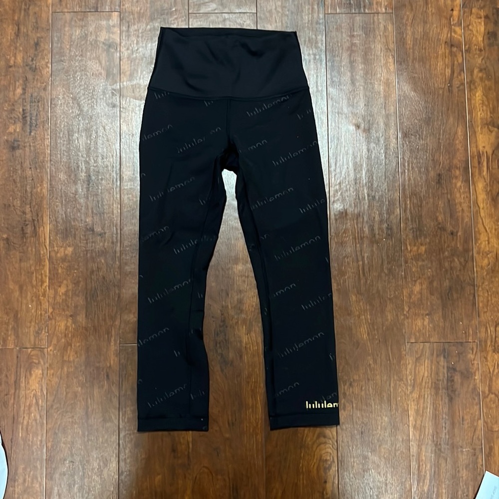 Never worn!! Lululemon cropped black leggings. With gold lulu symbol!